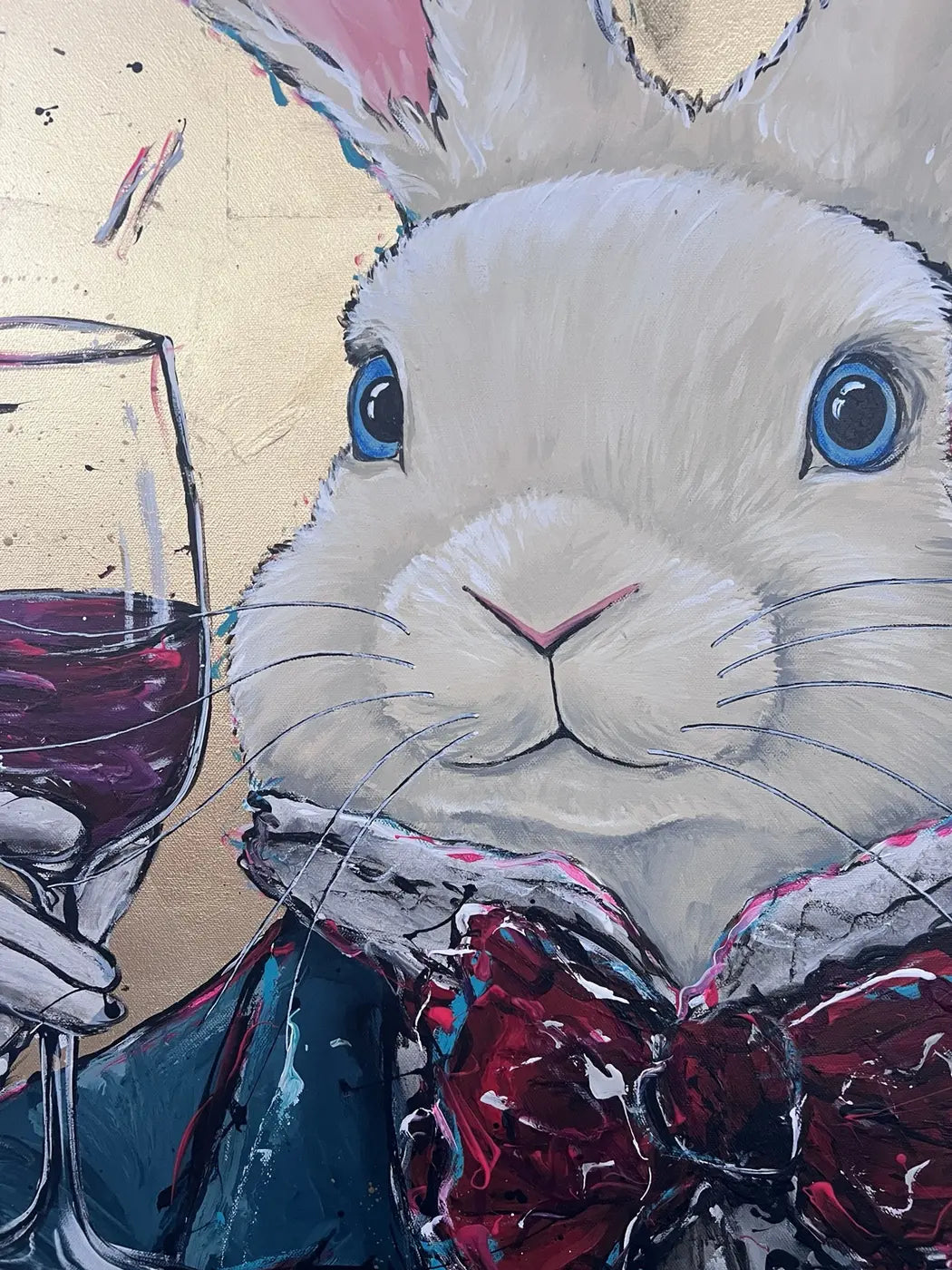Close-up of the white rabbit’s blue eyes, painted fur, wine glass and layered bow tie in Never too late – Party time.